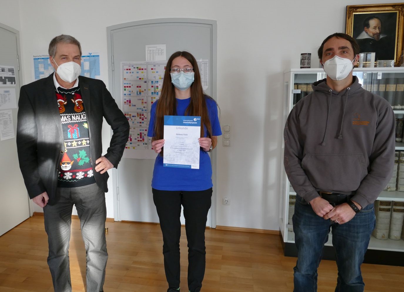 Beitrag-IChO202202 Urkundenübergabe kurz vor Weihnachten. V. l. n. r.: Schulleiter Hr. Wagner mit Jahreszeitlich passendem Pulli, Helena Fein, betreuender Lehrer Hr. Hausladen